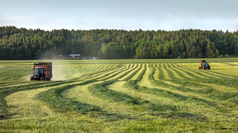 Tractors cutting rows across a green field at dusk.