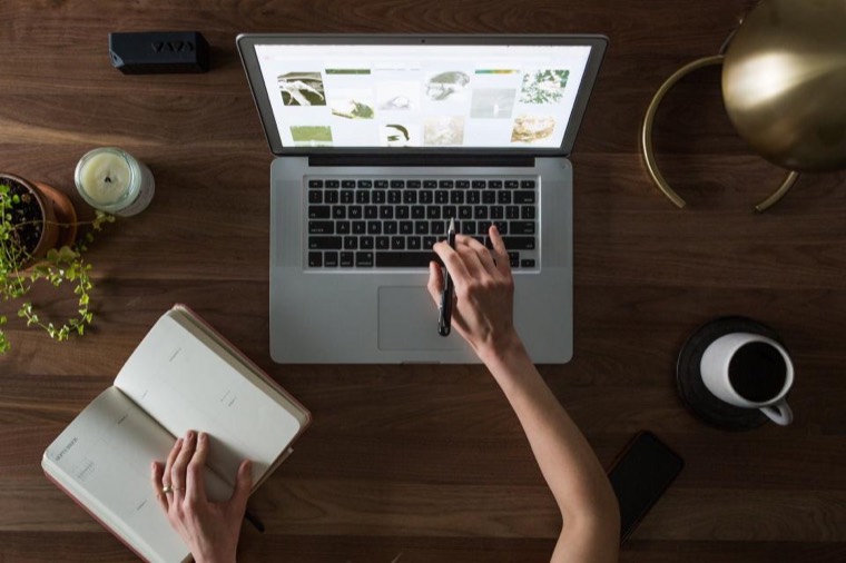 An overhead view of a person studying at a laptop with an open notebook beside it.